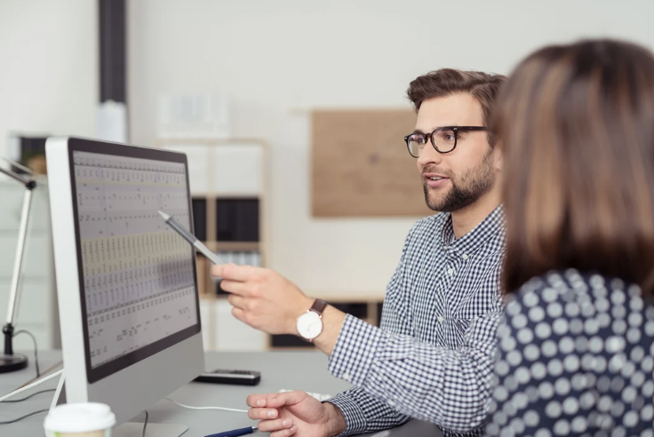 A man and woman analyzing data on a computer screen, representing the support team of UnionWare, a leading labor union app. 