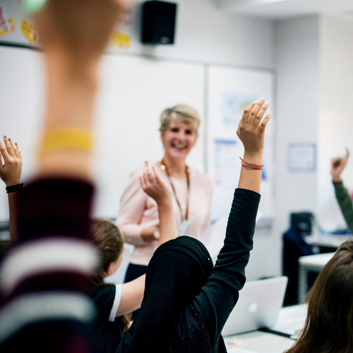 teacher-in-classroom-students-all-raising-hands